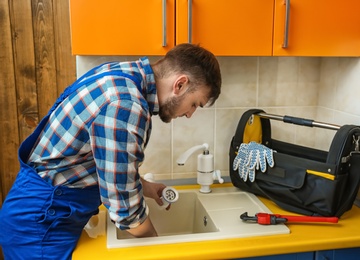 Professional plumber in uniform fixing kitchen sink