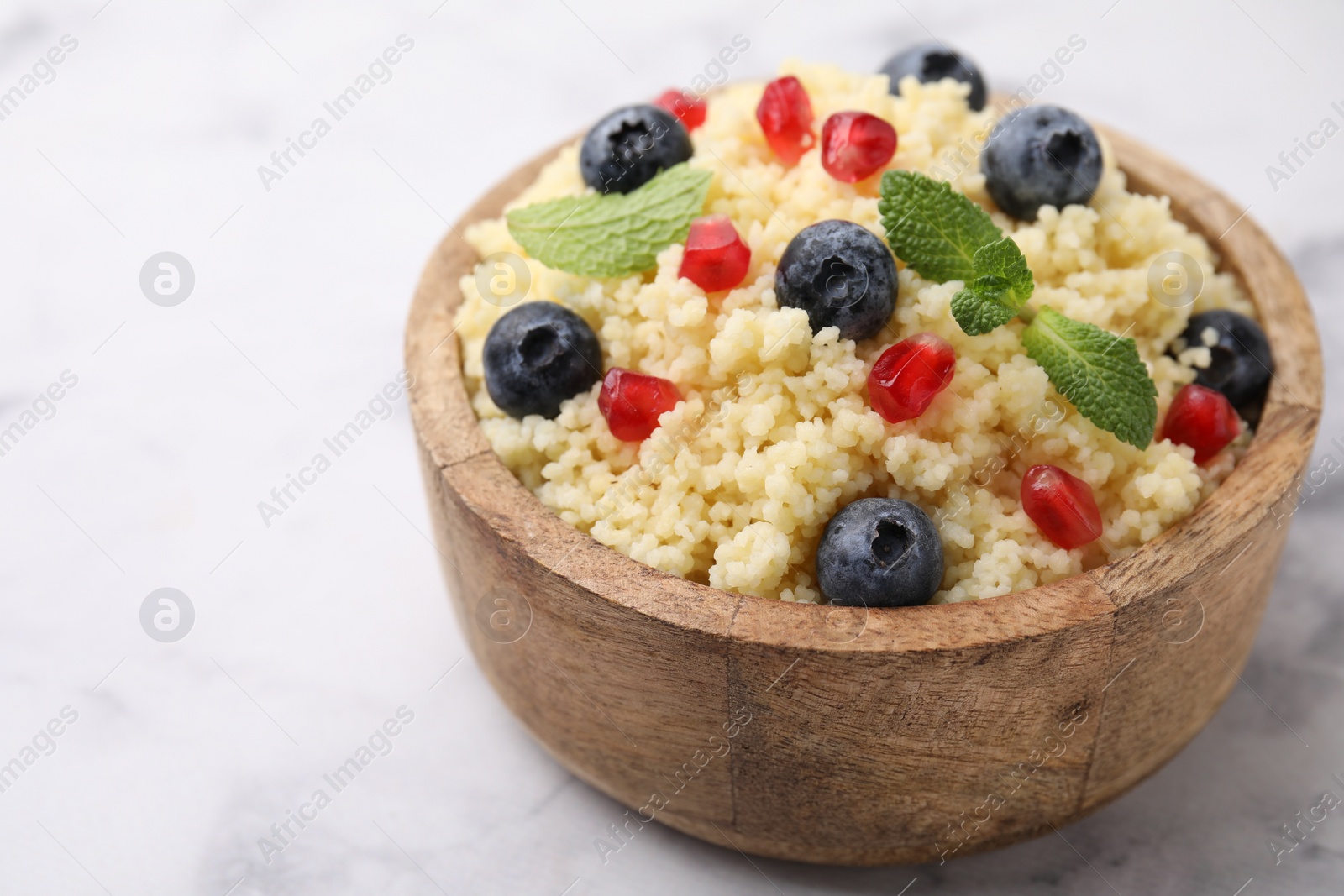 Photo of Bowl of tasty couscous with blueberries, pomegranate and mint on white marble table, closeup. Space for text
