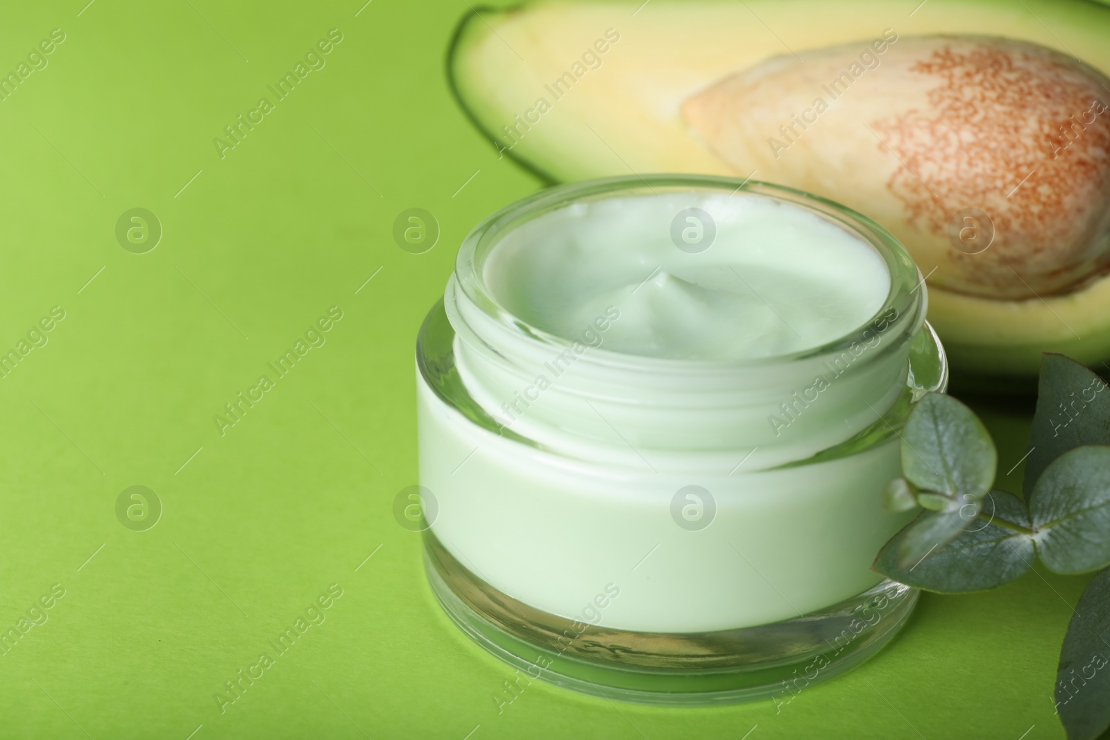 Photo of Jar of body cream with eucalyptus and avocado on light green background, closeup