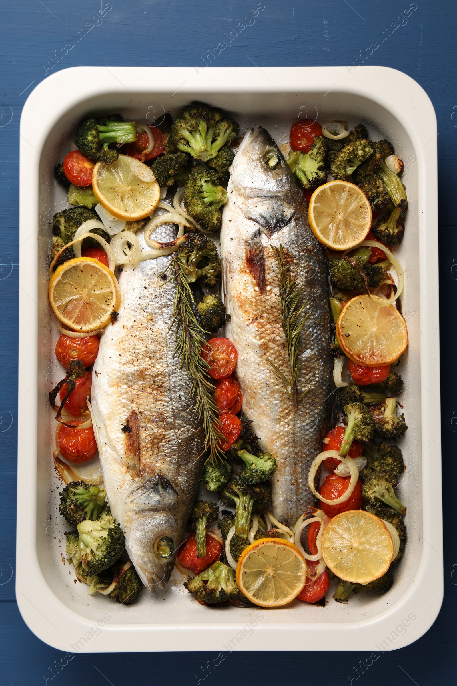 Photo of Delicious fish with vegetables and lemon in baking dish on blue wooden table, top view