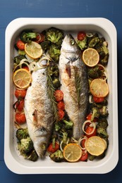 Photo of Delicious fish with vegetables and lemon in baking dish on blue wooden table, top view