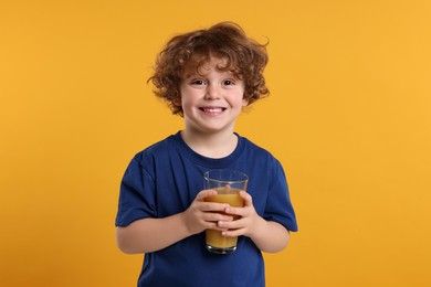 Photo of Cute little boy with glass of fresh juice on orange background