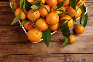 Fresh tangerines with green leaves in crate on wooden table, top view. Space for text