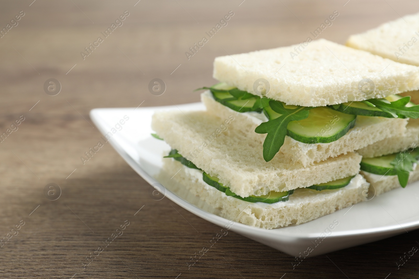 Photo of Plate with cucumber sandwiches on wooden table, closeup. Space for text