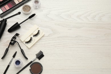Flat lay composition with eyelash curler, makeup products and accessories on white wooden table. Space for text