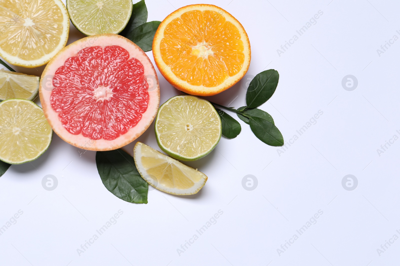 Photo of Different cut citrus fruits and leaves on white table, flat lay. Space for text