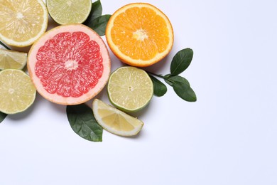 Different cut citrus fruits and leaves on white table, flat lay. Space for text