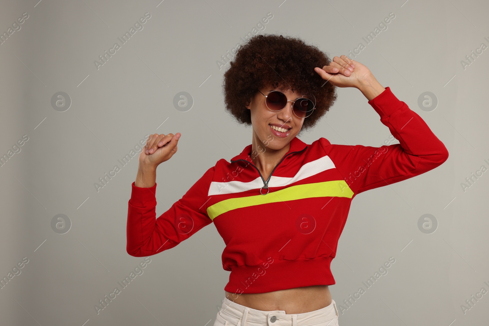 Photo of Happy young woman in stylish sunglasses dancing on grey background