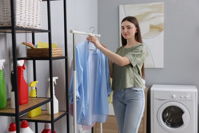 Beautiful young woman taking shirt from rack in laundry room