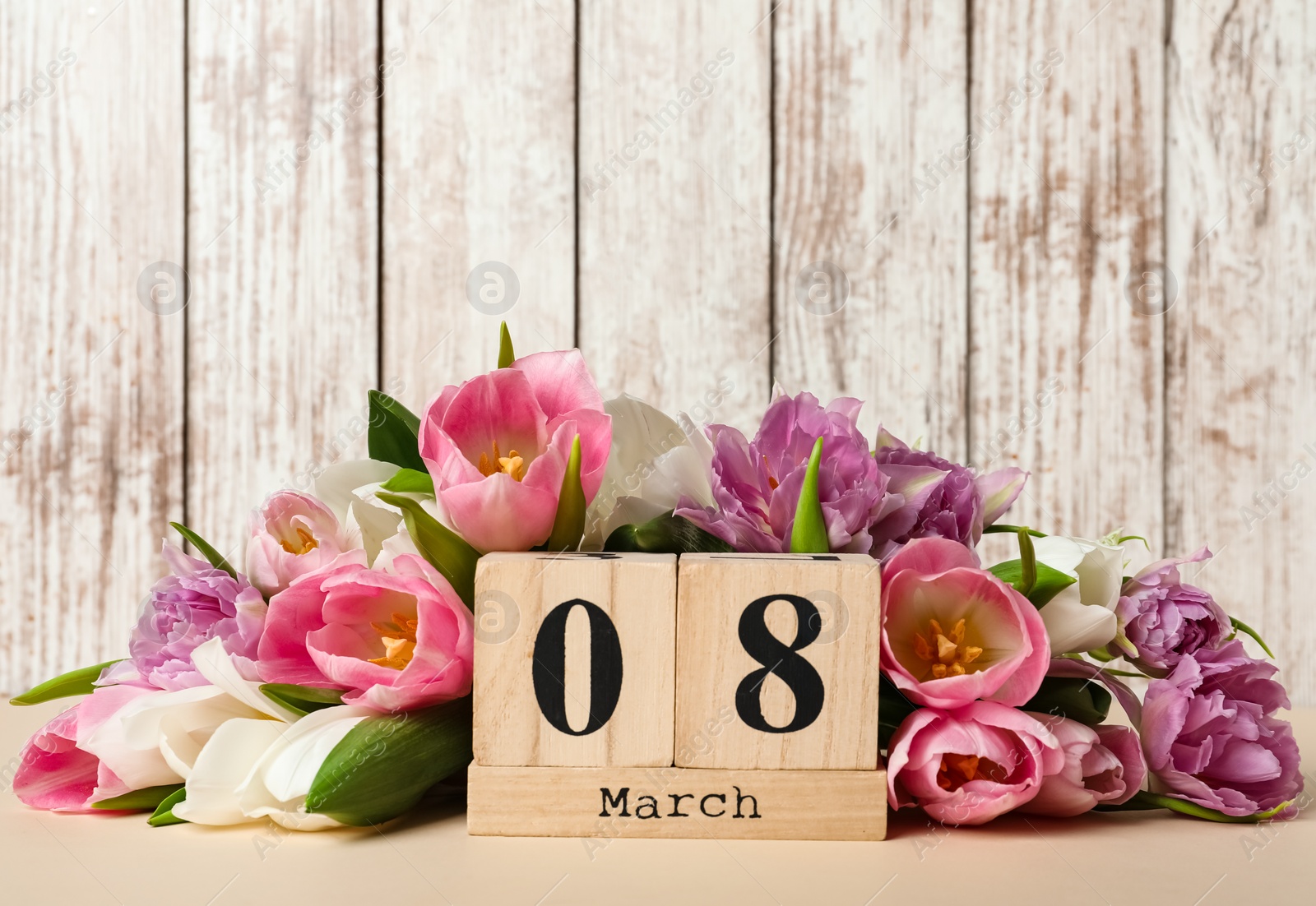 Photo of Block calendar with date 8th of March and tulips on table against wooden background, space for text. International Women's Day