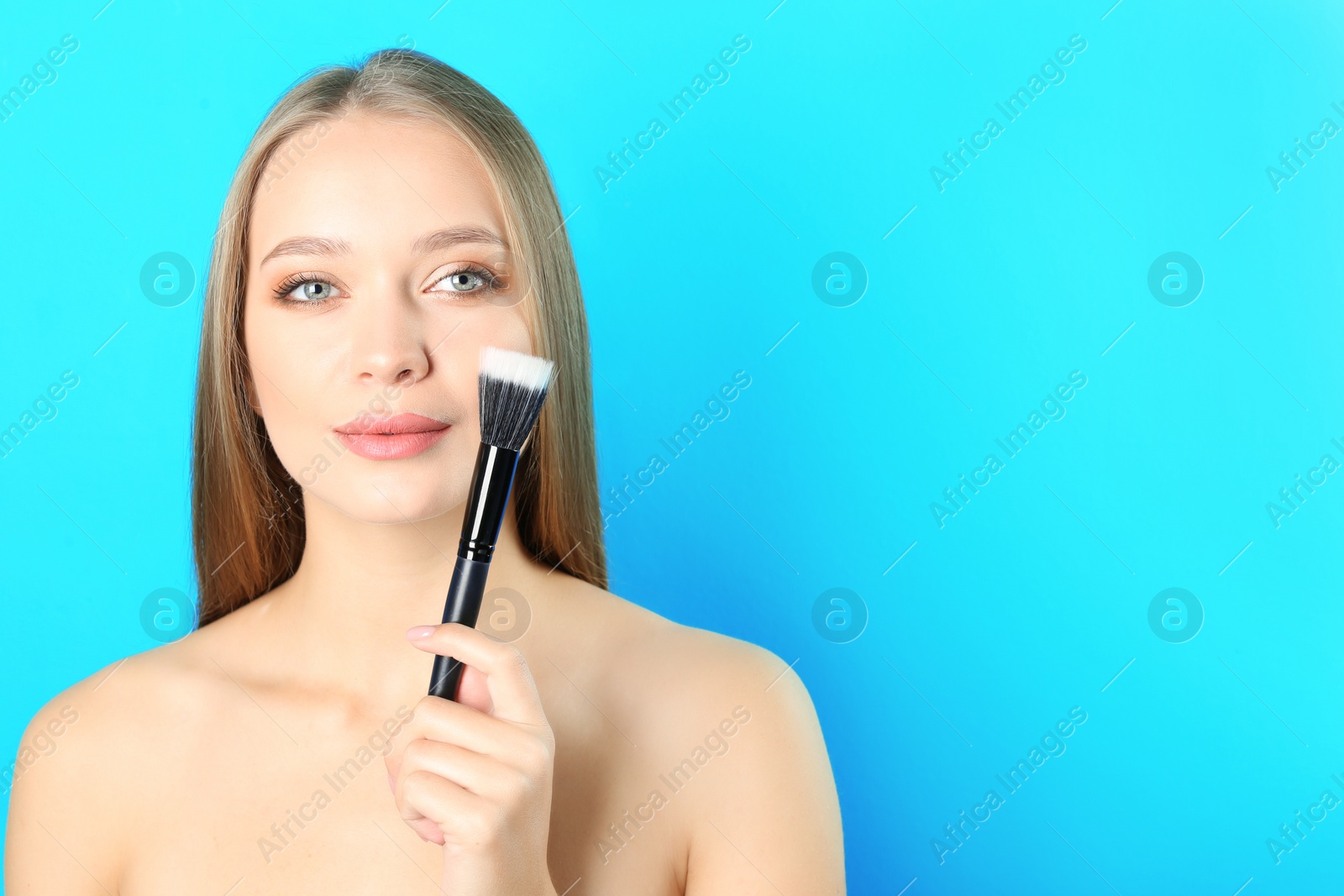 Photo of Portrait of beautiful young woman with makeup brush on color background. Space for text