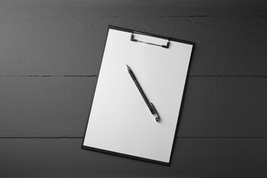 Photo of Clipboard with sheet of paper and pen on black wooden table, top view