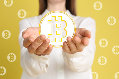 Fintech concept. Woman demonstrating bitcoin symbol on yellow background