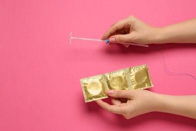 Photo of Woman holding condoms and intrauterine device on light pink background, top view. Choosing birth control method