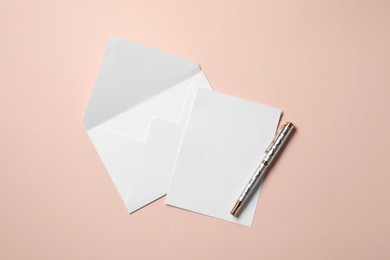 Blank sheet of paper, letter envelope and pen on beige background, top view. Space for text