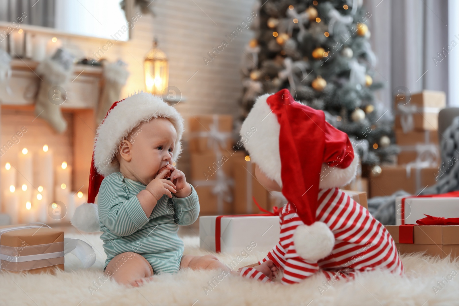 Image of Cute children in Santa hats on floor in room with Christmas tree