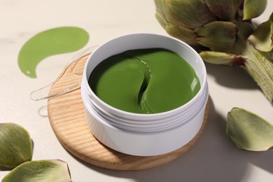 Photo of Package of under eye patches and artichoke on white table, closeup. Cosmetic product