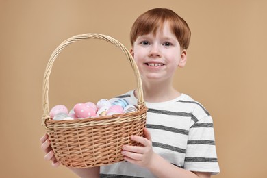 Photo of Easter celebration. Cute little boy with wicker basket full of painted eggs on dark beige background