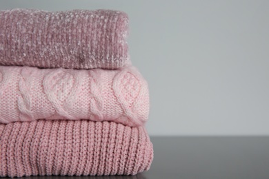 Photo of Stack of folded knitted sweaters on grey table, closeup. Space for text