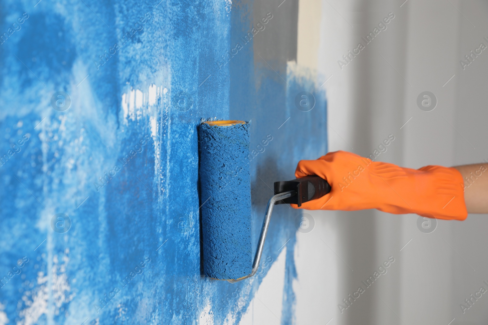 Photo of Woman painting white wall with blue dye, closeup