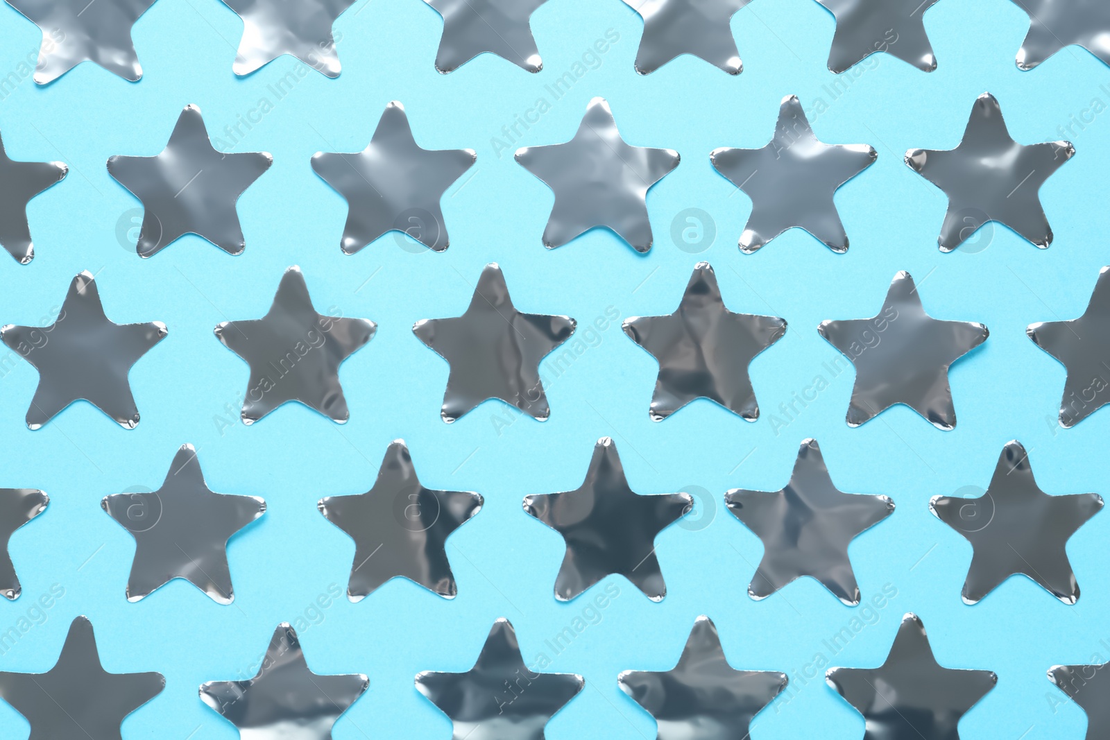 Photo of Shiny silver star shaped confetti on light blue background, flat lay