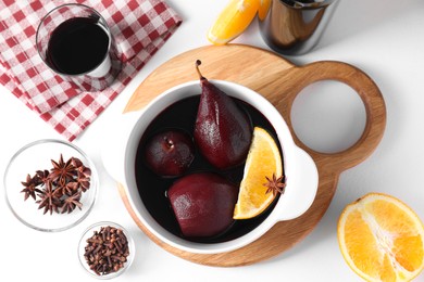 Tasty red wine poached pears in pot, orange and spices on white table, flat lay