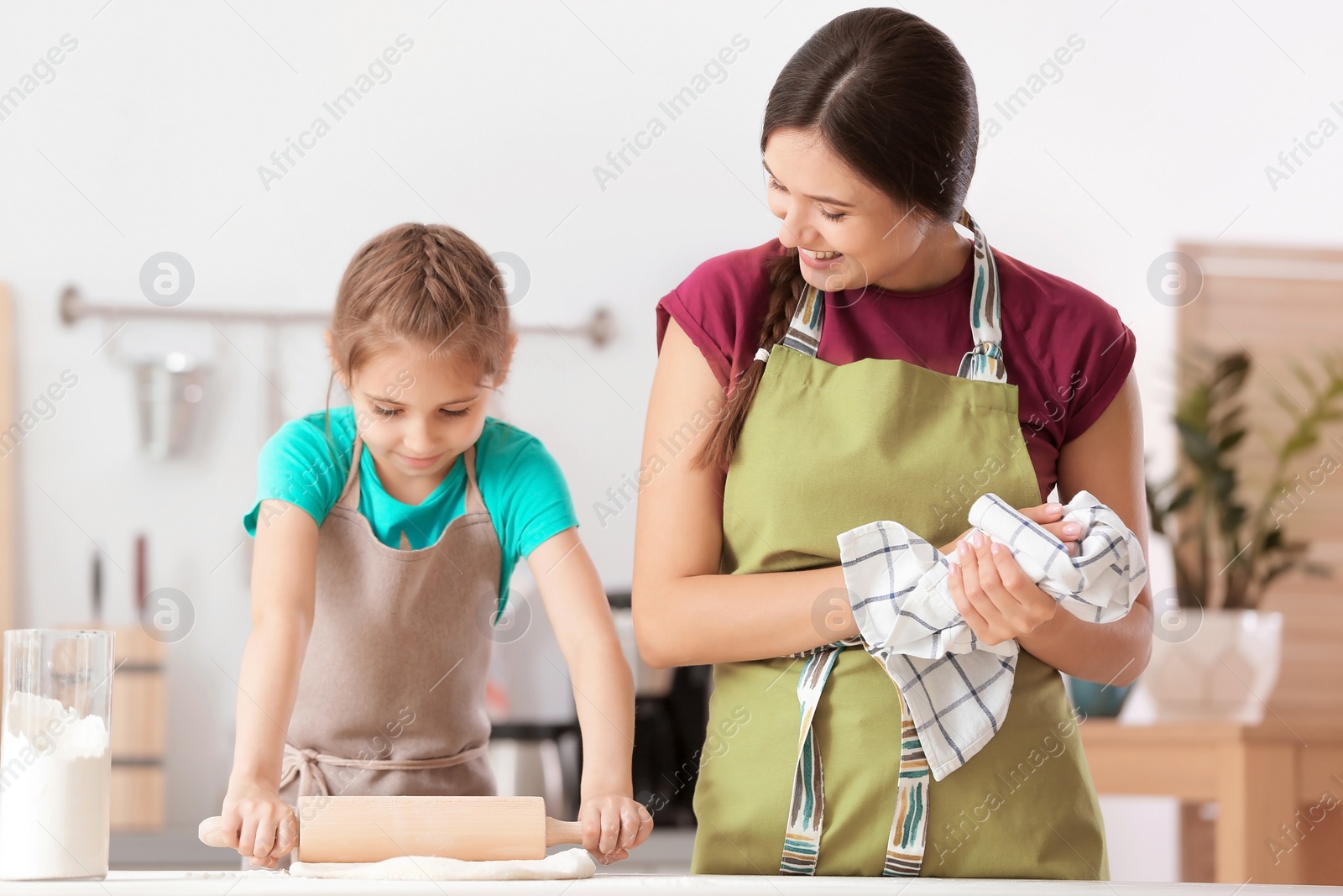 Photo of Mother and her daughter preparing dough at table in kitchen