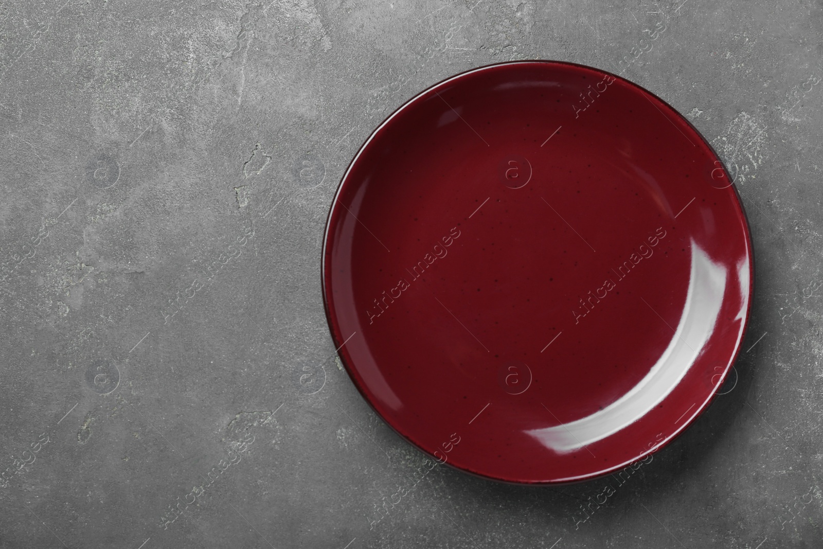 Photo of Empty burgundy ceramic plate on grey table, top view. Space for text