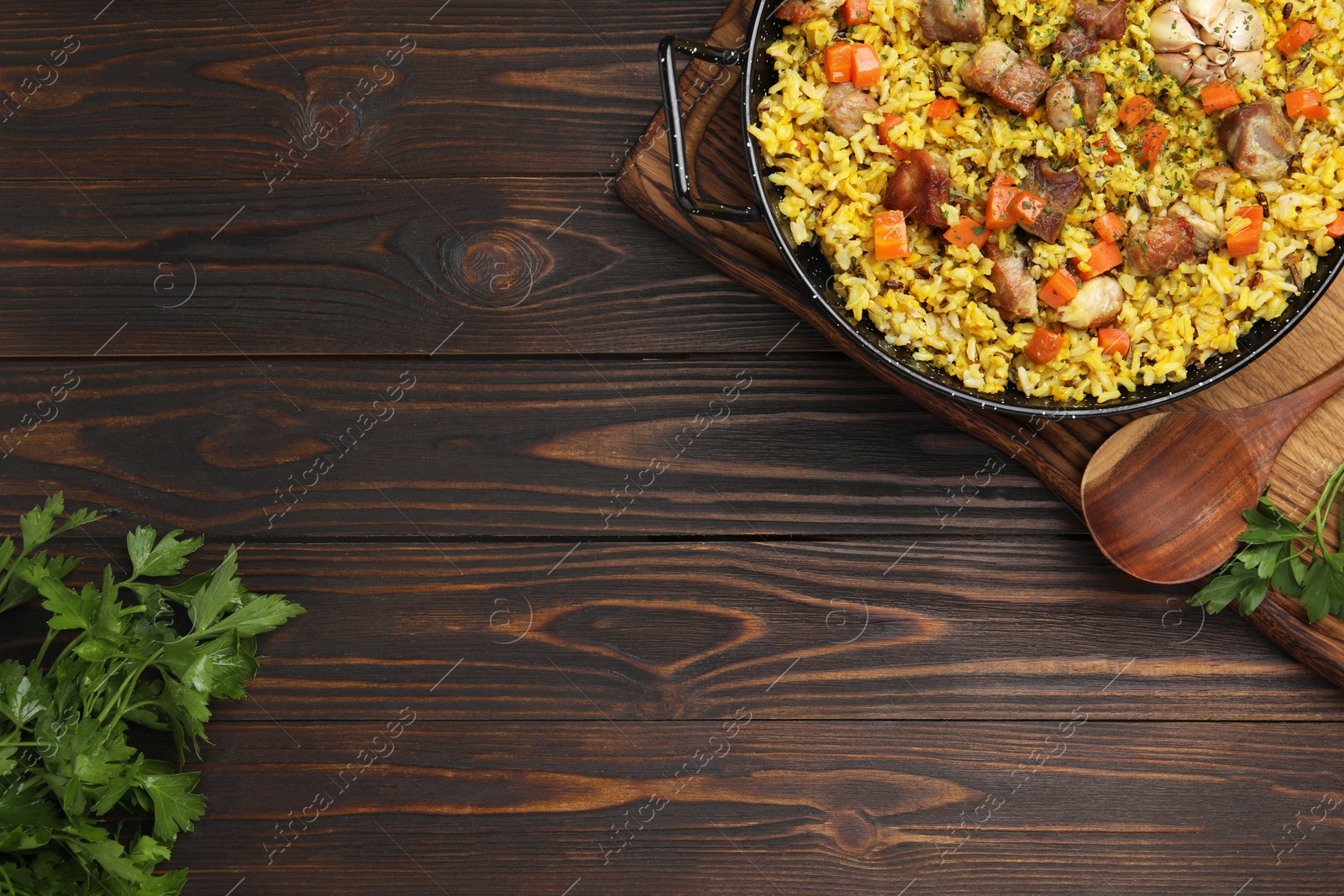 Photo of Delicious pilaf with meat, carrot and garlic served on wooden table, flat lay. Space for text