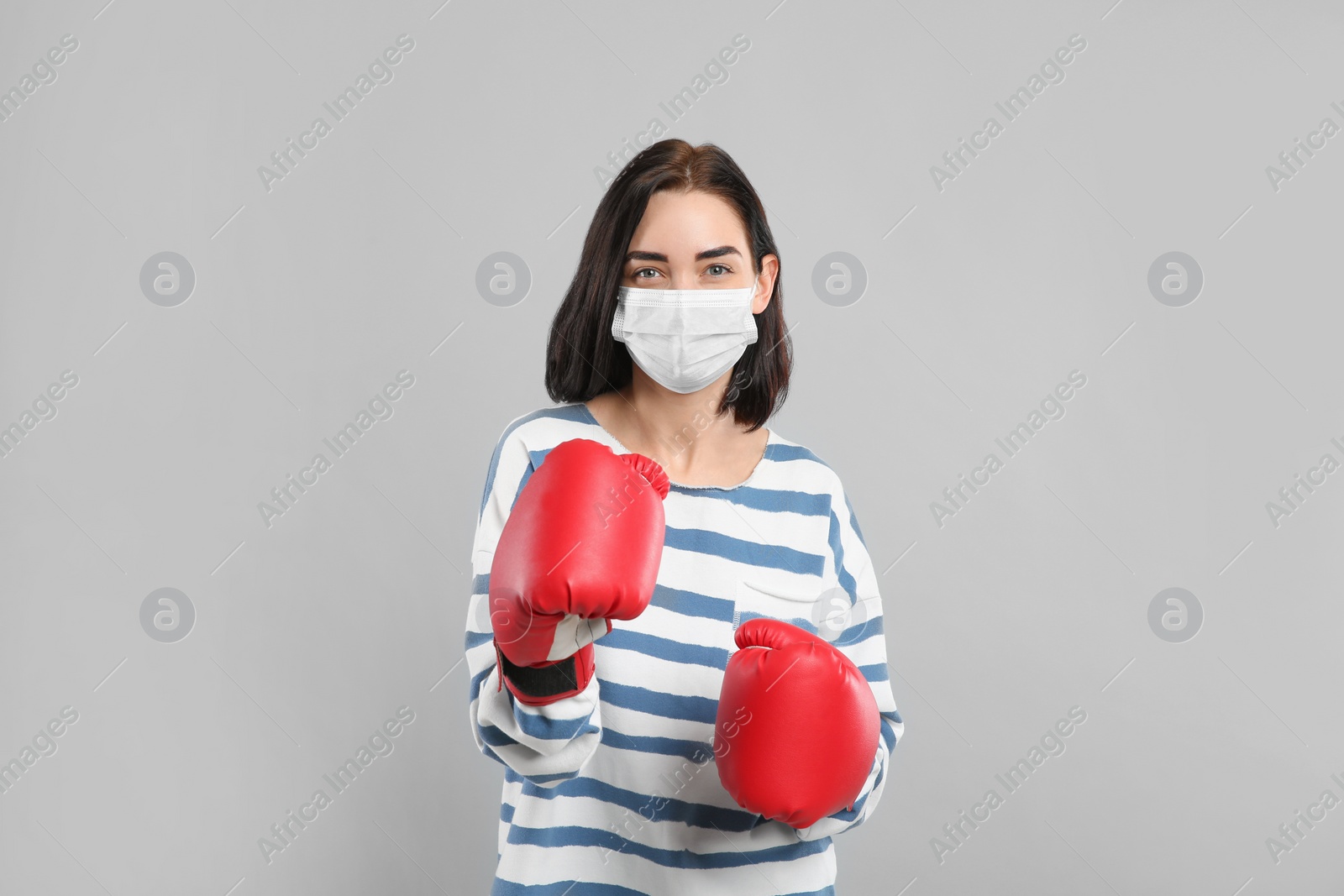 Photo of Woman with protective mask and boxing gloves on light grey background. Strong immunity concept