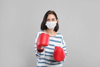 Woman with protective mask and boxing gloves on light grey background. Strong immunity concept