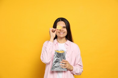 Beautiful woman holding potato chips near eye on orange background