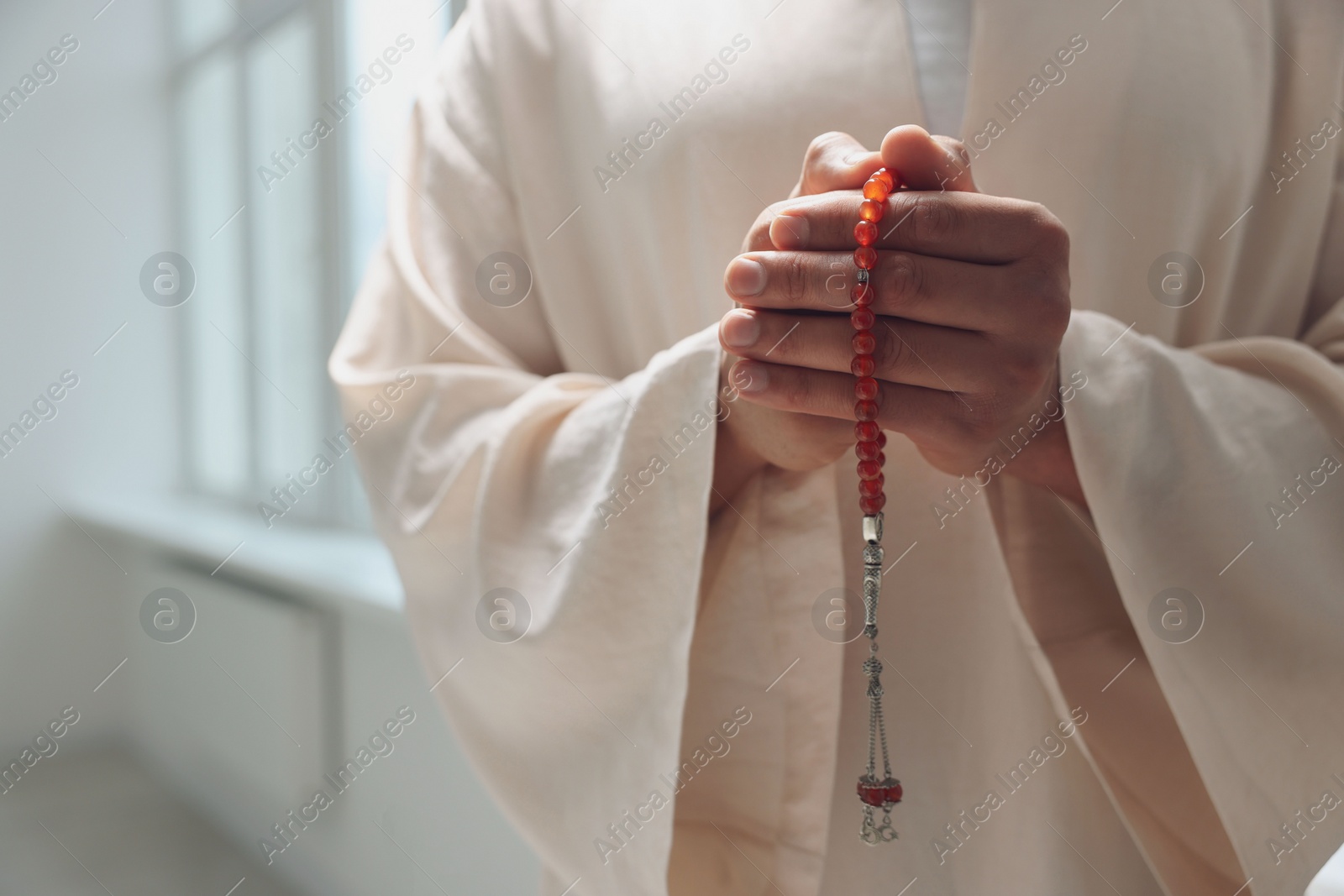 Photo of Muslim man with misbaha praying indoors, closeup