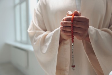 Photo of Muslim man with misbaha praying indoors, closeup