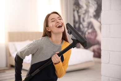 Photo of Young woman having fun while vacuuming at home