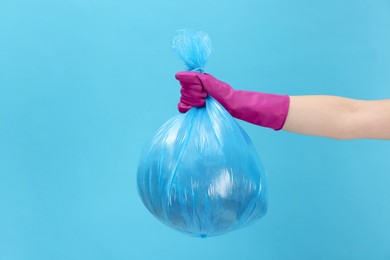 Photo of Woman holding plastic bag full of garbage on light blue background, closeup