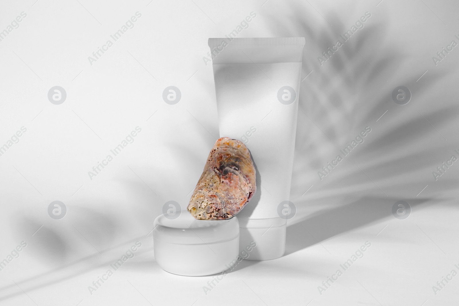 Photo of Cosmetic products, quartz gemstone and shadow of tropical leaf on white background