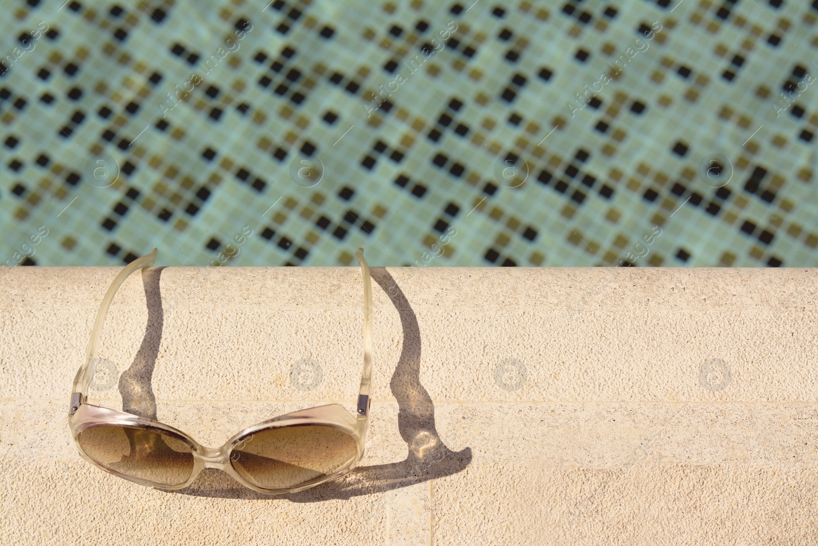 Photo of Stylish sunglasses near outdoor swimming pool on sunny day