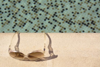 Stylish sunglasses near outdoor swimming pool on sunny day