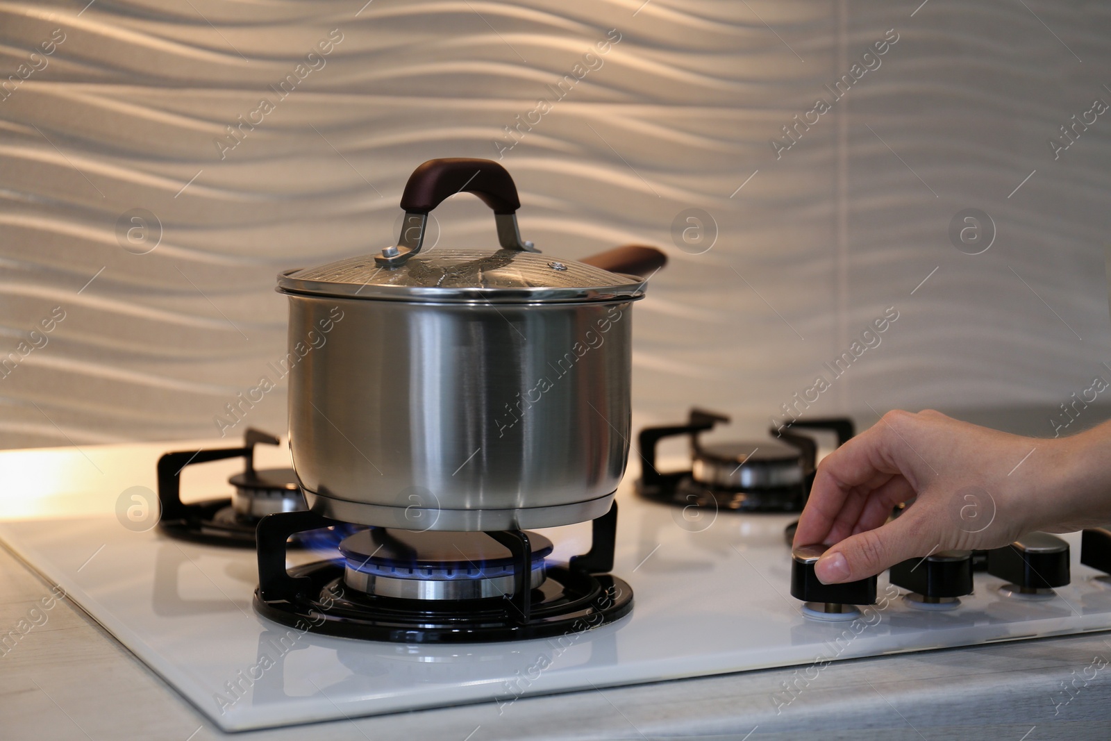 Photo of Woman cooking food in pot on modern kitchen stove with burning gas indoors, closeup