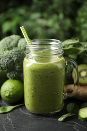 Photo of Delicious green juice and fresh ingredients on black table