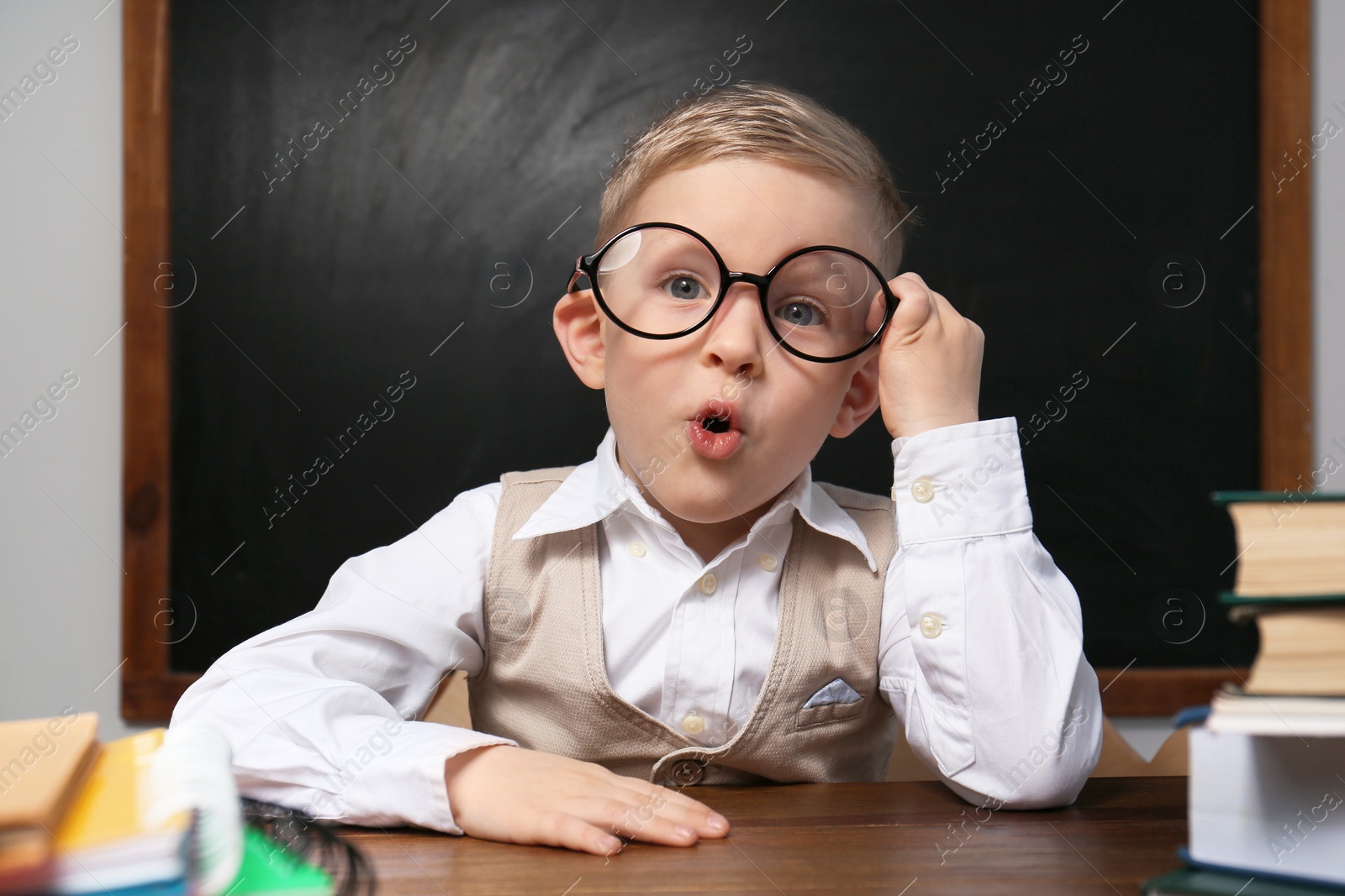 Photo of Cute little child wearing glasses at desk in classroom. First time at school