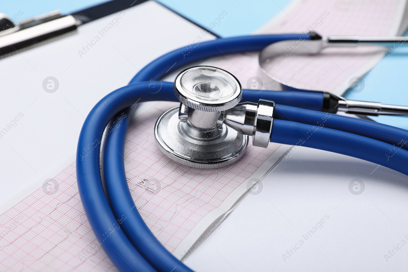 Photo of Stethoscope, clipboard and cardiogram paper on light blue background, closeup