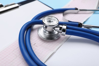 Photo of Stethoscope, clipboard and cardiogram paper on light blue background, closeup