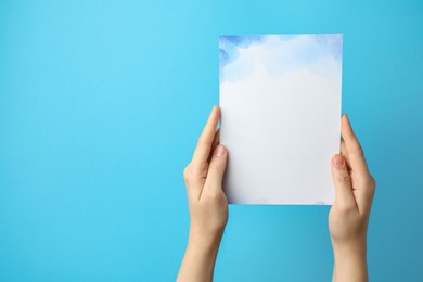 Photo of Woman holding blank invitation card on light blue background, closeup. Space for text
