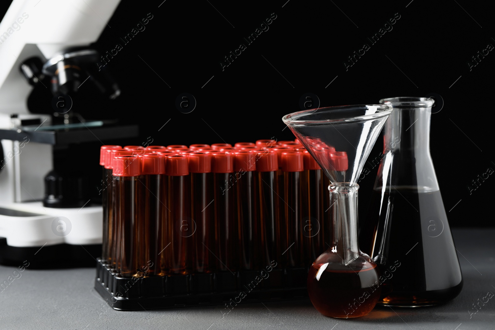 Photo of Different laboratory glassware with brown liquids on grey table