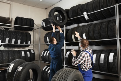 Young male mechanics with car tires in automobile service center