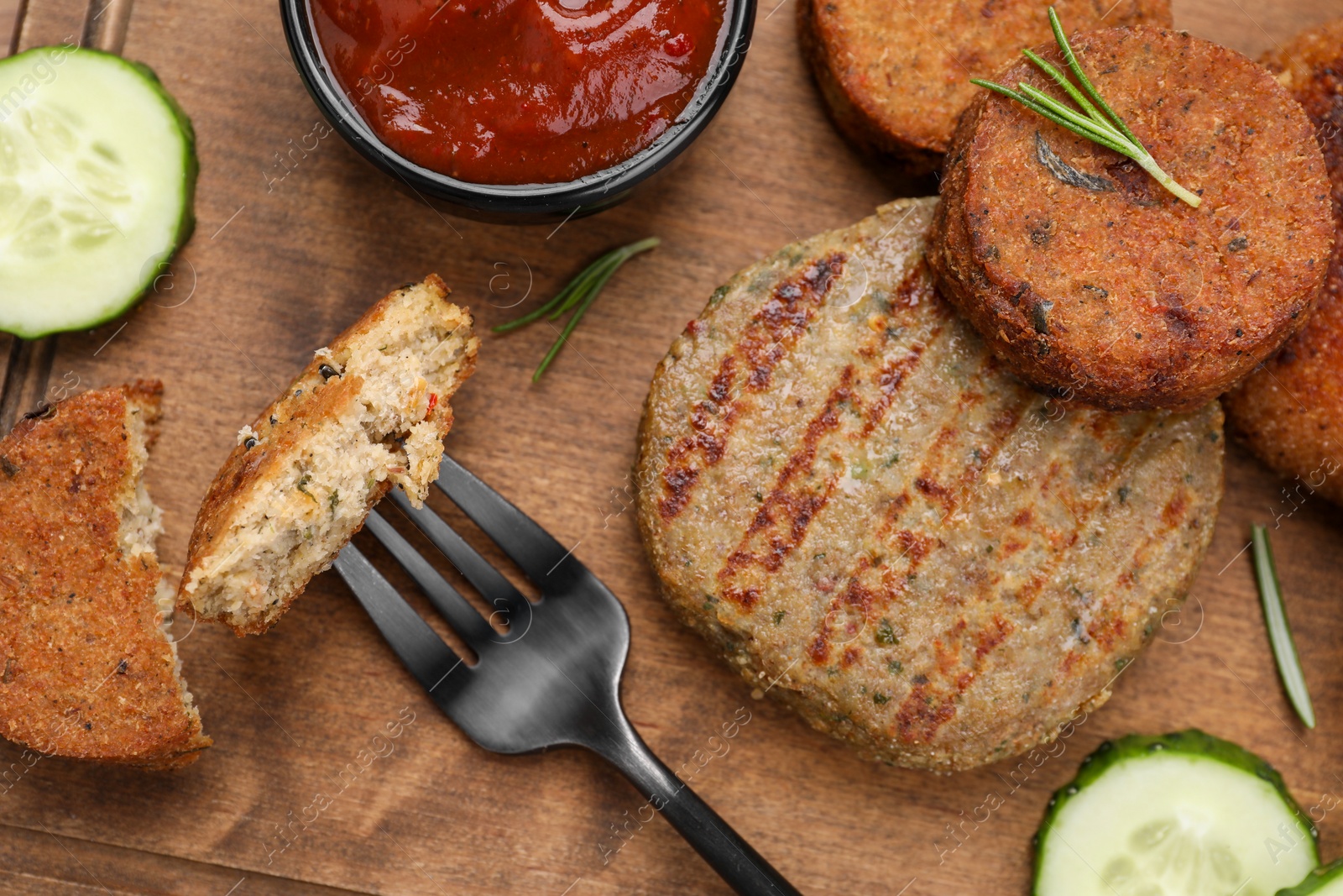 Photo of Fork with piece of delicious cutlet near tasty vegan meat products and sauce on wooden table, flat lay