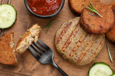 Photo of Fork with piecedelicious cutlet near tasty vegan meat products and sauce on wooden table, flat lay