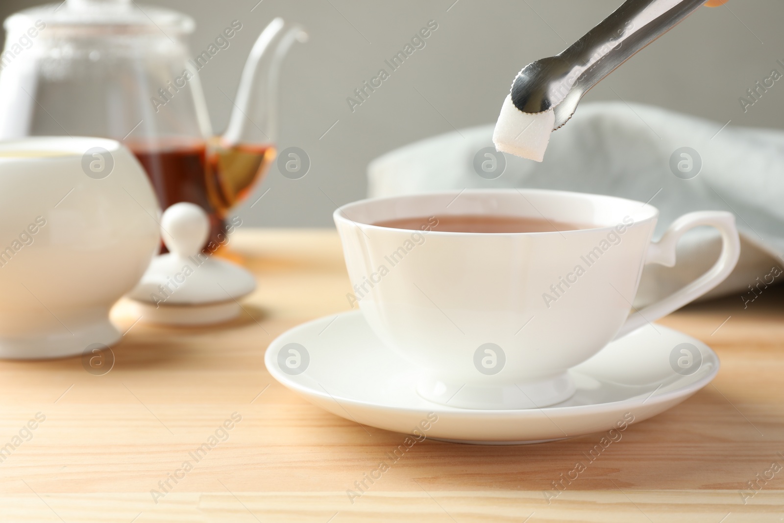 Photo of Adding sugar cube into cup of tea at wooden table, closeup